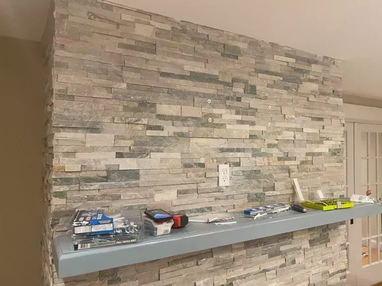 Stone accent wall with a long gray shelf holding assorted small items in a room