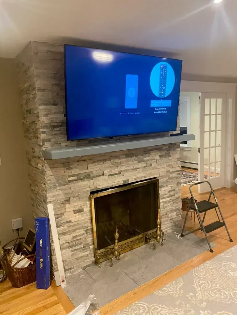Living room fireplace with mounted TV, stone mantel, and two folding chairs nearby