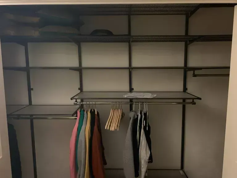 Empty walk-in closet with shelves and hanging clothes, mostly dark metal shelving and a few garments on the rack