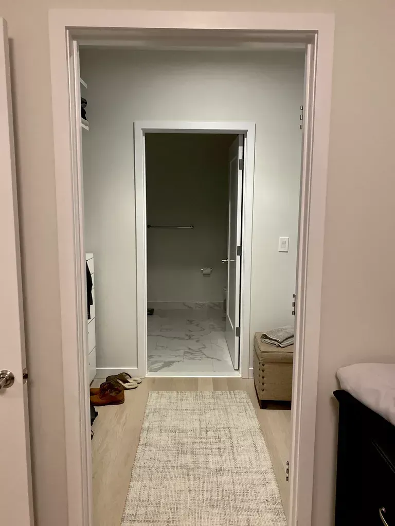 View through a doorway into a bedroom hallway with a long beige rug and an open bathroom beyond.