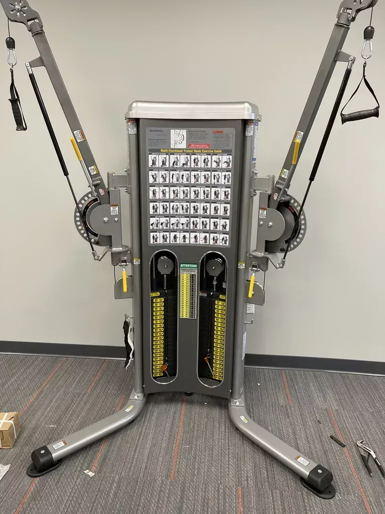 Gym cable machine with adjustable arms and weight stacks in a fitness room.