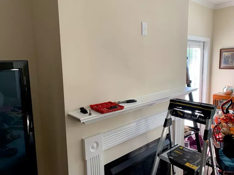 Living room with white mantel, TV on left, and a red toolbox on the shelf above a fireplace.