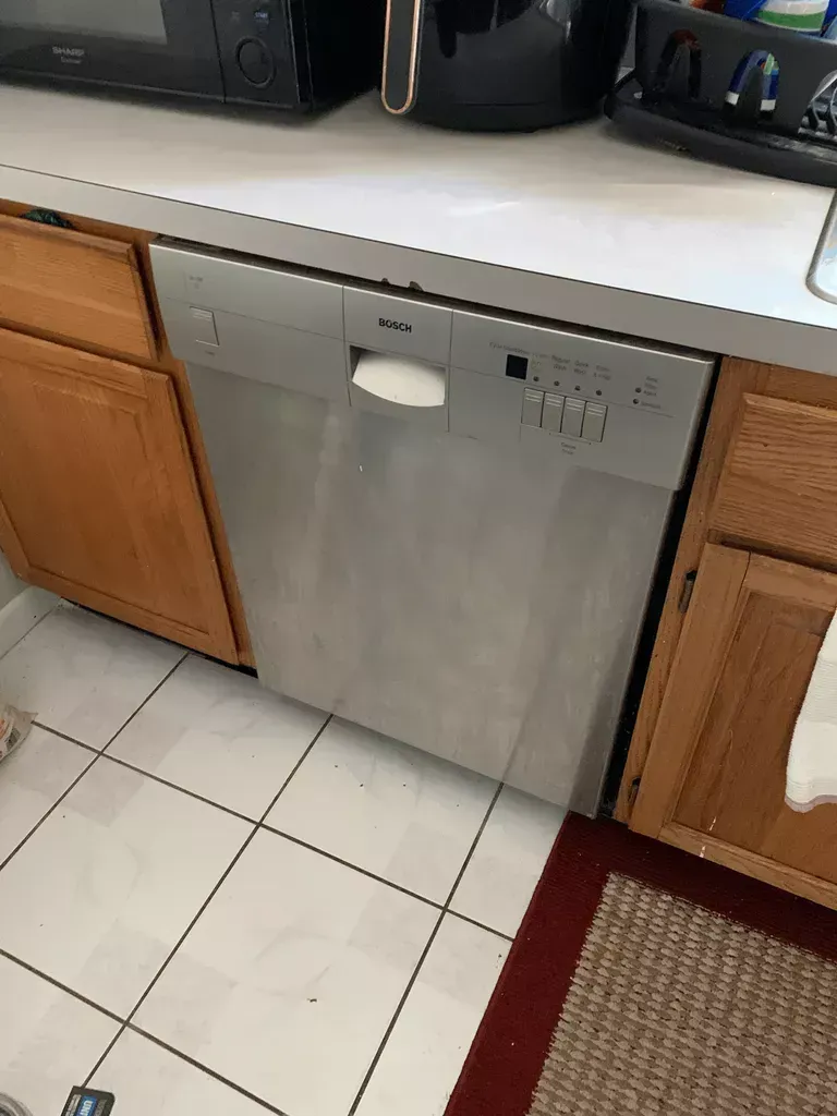 Stainless steel dishwasher under a kitchen counter with wooden cabinets and tile floor