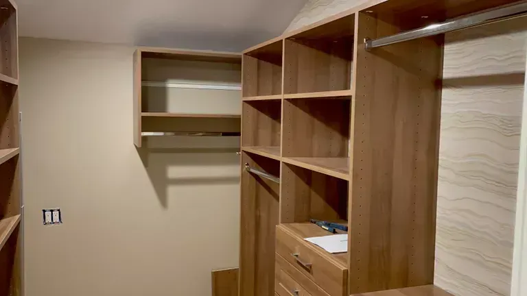 Built-in wooden closet and shelving in a beige room, with drawers and open hanging space.