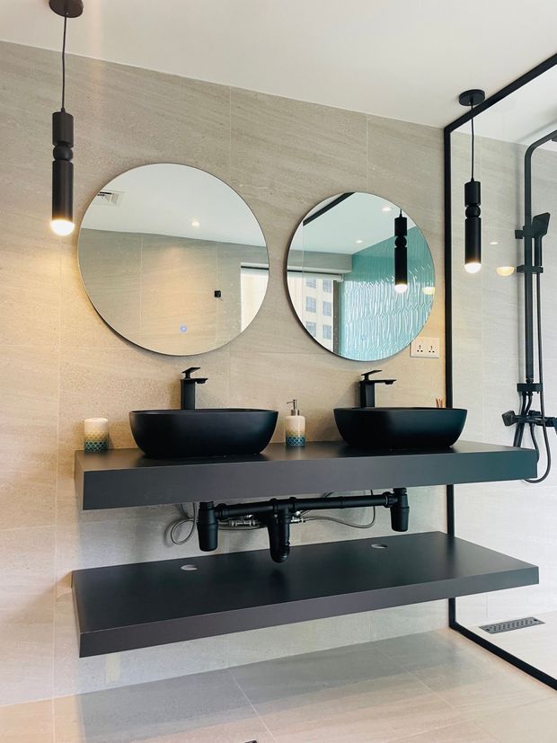 Modern bathroom with double black vessel sinks, round mirrors, floating shelves, and glass shower enclosure