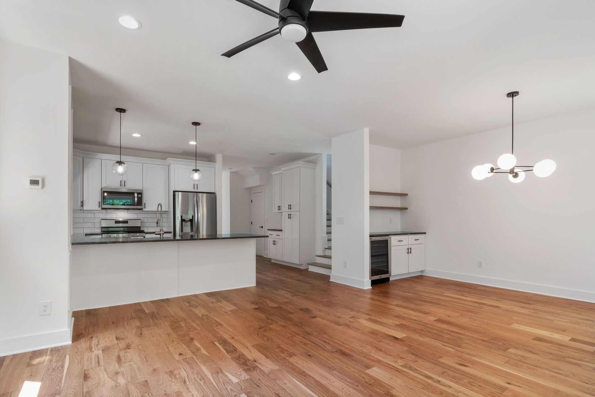 Open-plan kitchen and living room with hardwood floors, white walls, ceiling fan, and pendant light.
