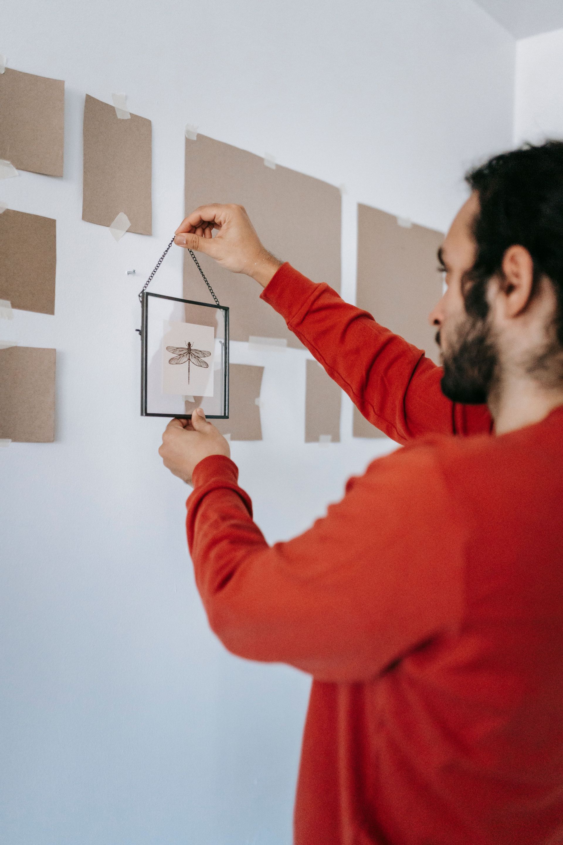 Person in red sweater hanging a framed print on a wall with brown paper templates