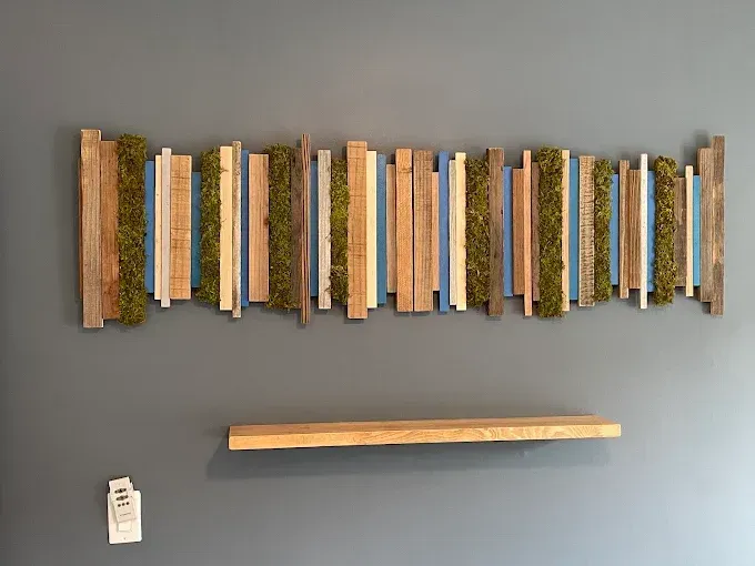 Wall-mounted slat art with colorful vertical strips above a wooden shelf on a gray wall