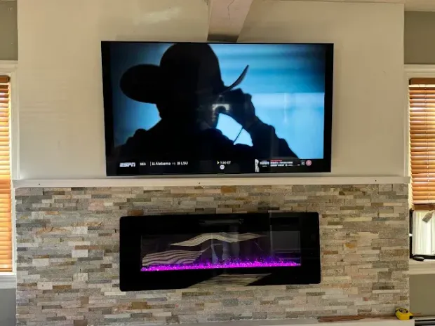 Living room wall with mounted TV showing a cowboy silhouette above a stone fireplace with purple flames