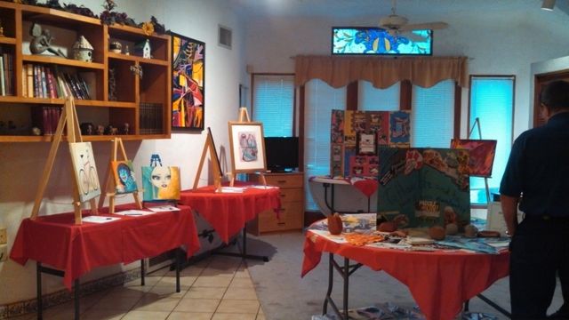 An art gallery with paintings on easels and tables covered in red cloth. A person stands on the right.