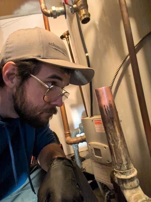 Technician inspecting copper pipes and a wall-mounted valve in a utility room