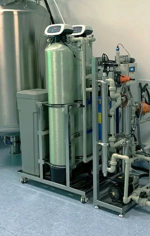 Industrial water filtration equipment with silver tanks, pipes, and gauges in a utility room
