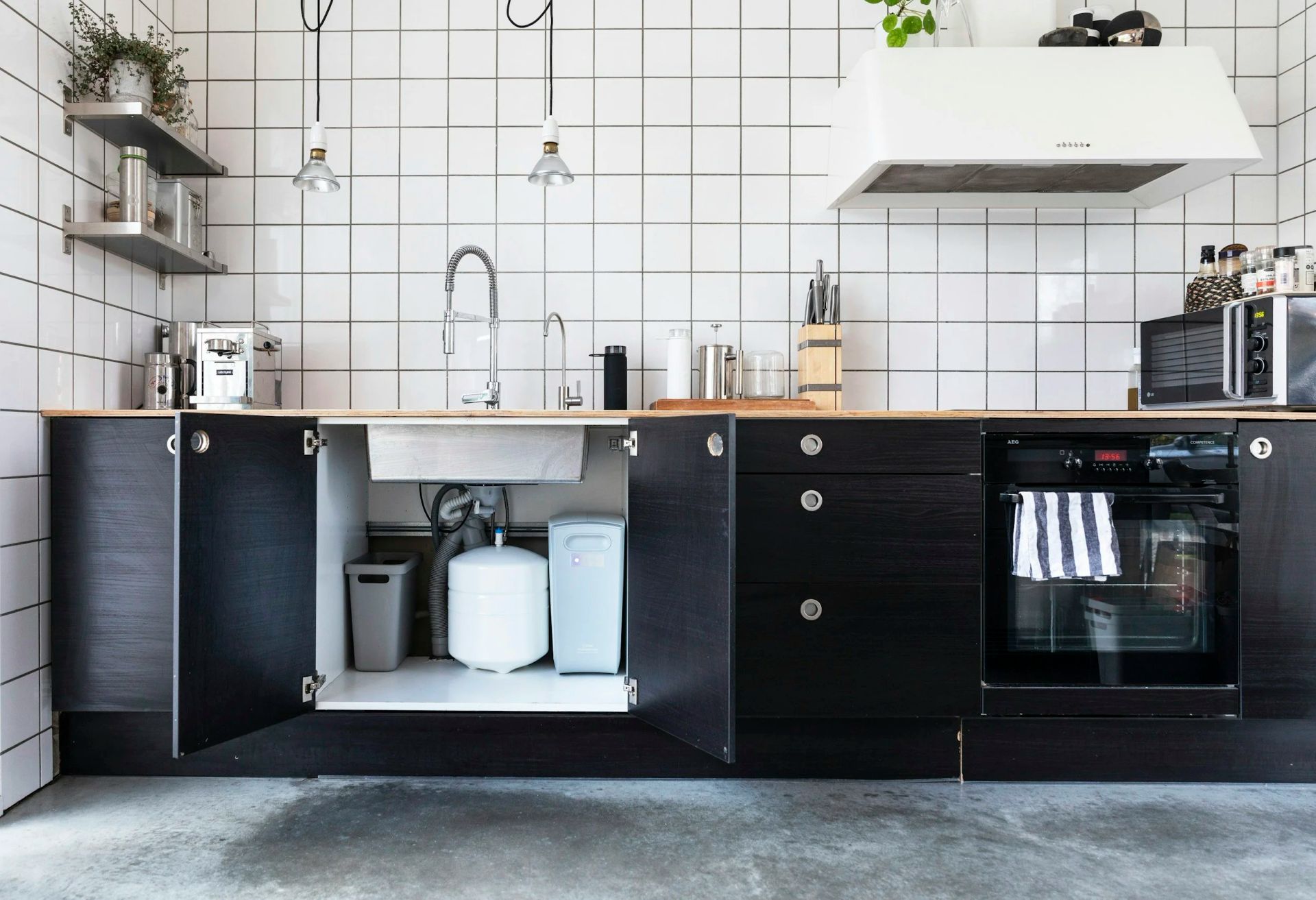 Modern black-and-white kitchen with tiled backsplash, sink, stove, and open lower cabinets.