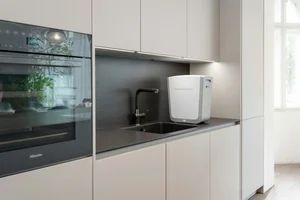 Modern kitchen with built-in oven, black countertop, and white appliances by a window