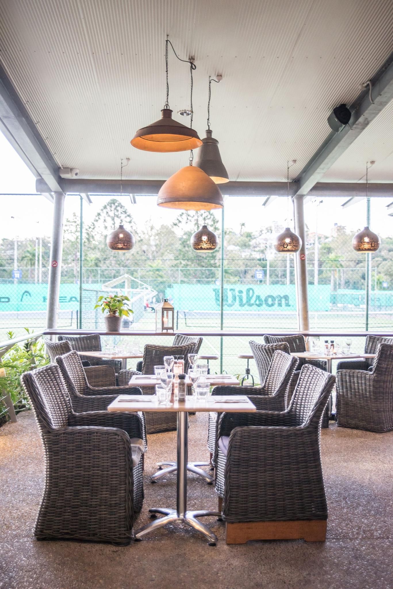 A restaurant with tables and chairs and a tennis court in the background