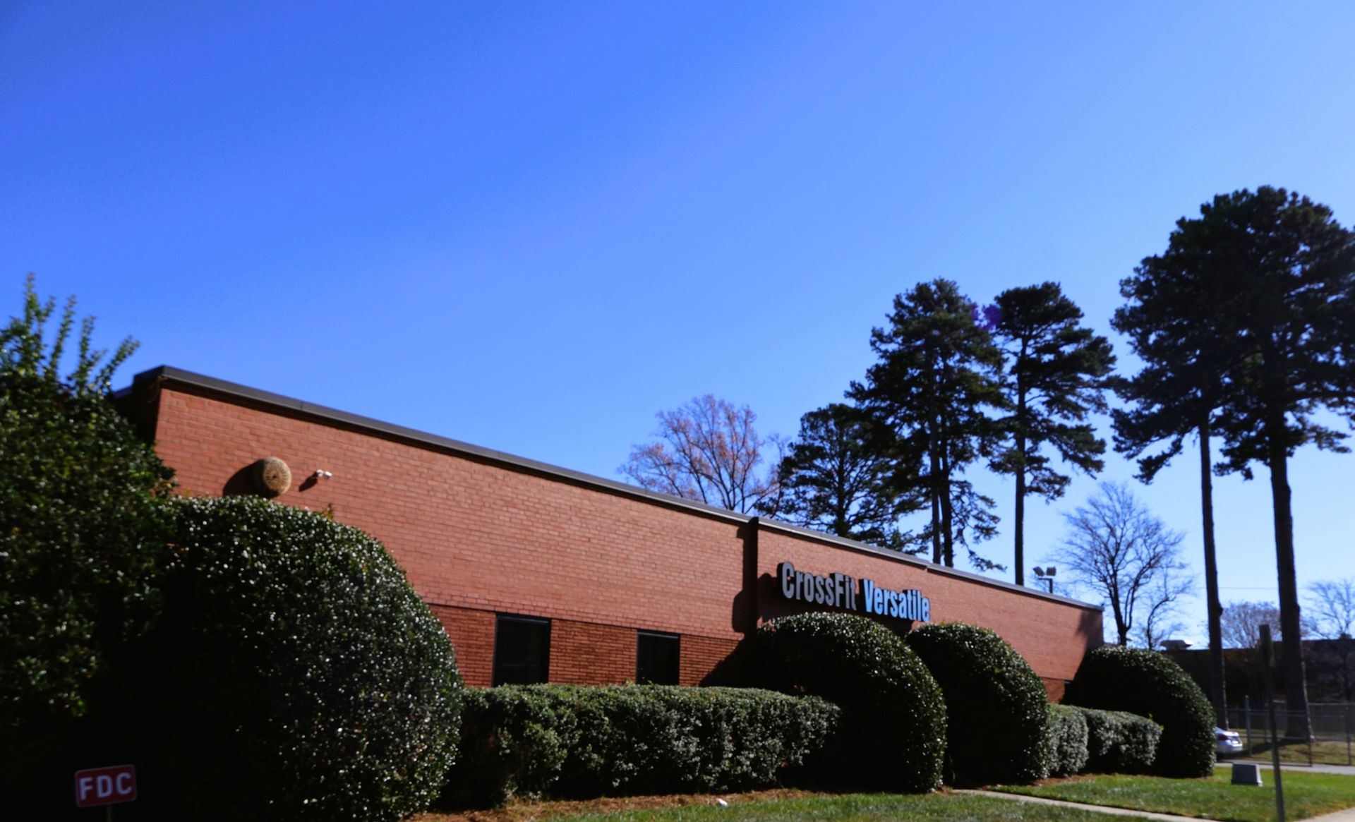 Red brick building with shrubs, trees, and blue sky.