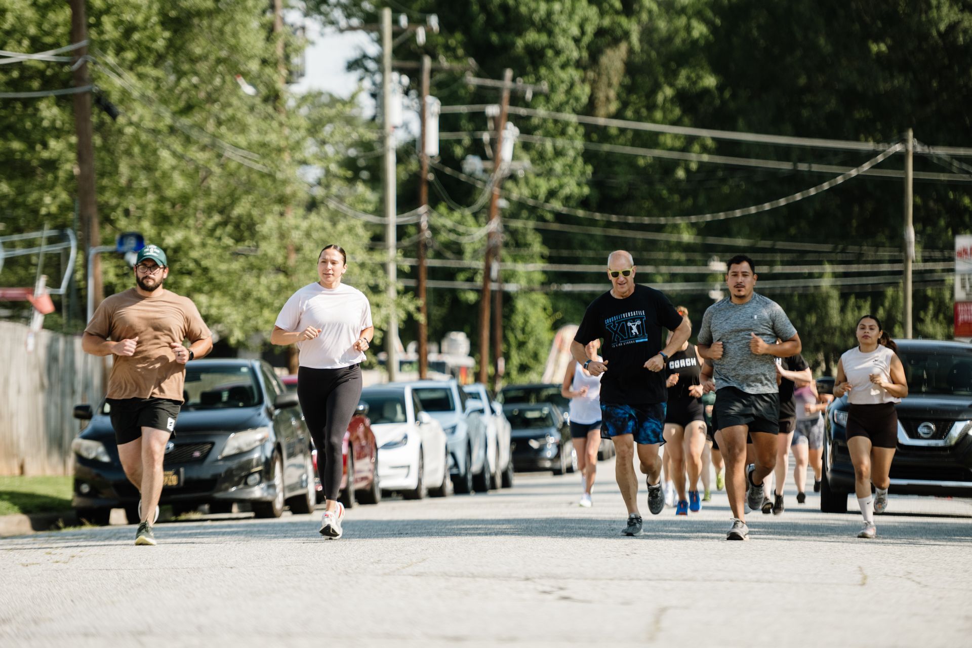 Group run organized by Greensboro NC gym with members running down city street. cars parked along the side