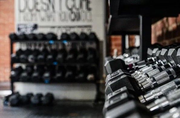 Rows of dumbbells on a rack in a gym, with text on a wall in the background.