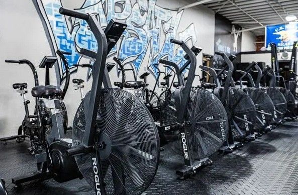 Row of black fan bikes in a gym with graffiti wall in the background.