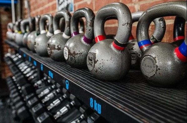 Row of gray kettlebells on a shelf, various weights marked, against a brick wall in CrossFit Versatile gym.