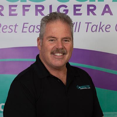 A man in a striped shirt is smiling in front of a sign.