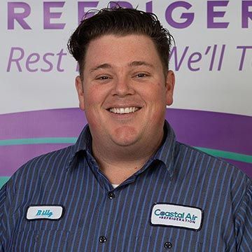 A man in a striped shirt is smiling in front of a sign.