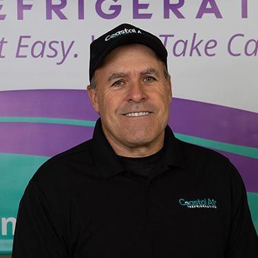 A man in a striped shirt is smiling in front of a sign.