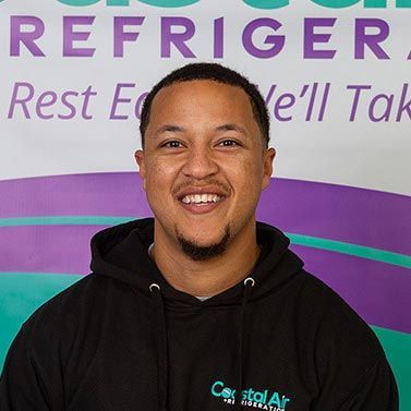 A man in a striped shirt is smiling in front of a sign.