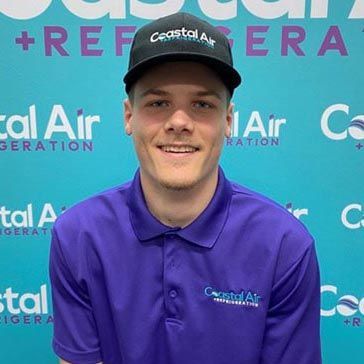 A man in a striped shirt is smiling in front of a sign.