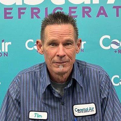 A man in a striped shirt is standing in front of a blue background.