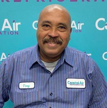 A man in a striped shirt is smiling in front of a sign.