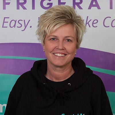 A woman is wearing a black hoodie and smiling in front of a sign.