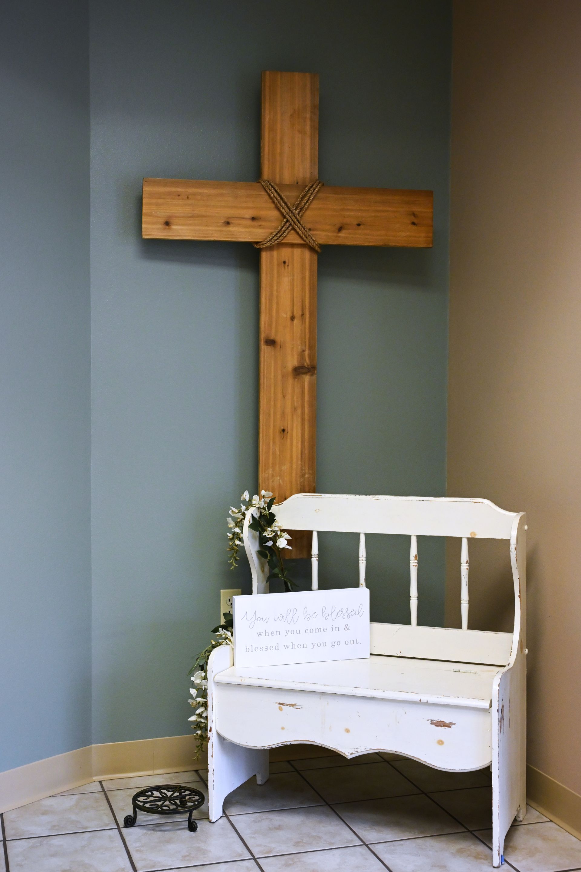 White chair beneath a wooden cross on a blue wall, in a small quiet room.