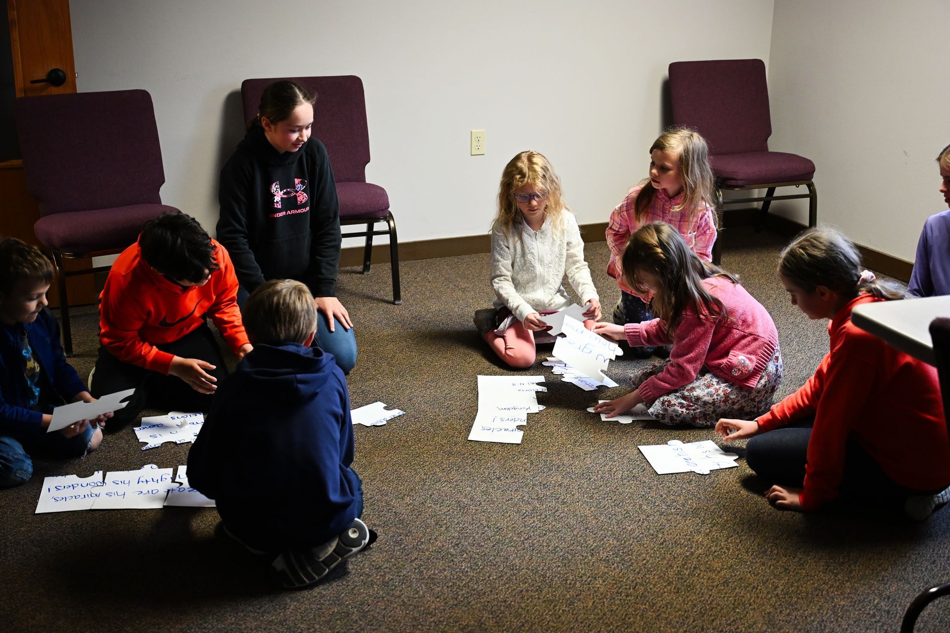 Children sitting in a circle on a carpet, looking at papers during a classroom activity