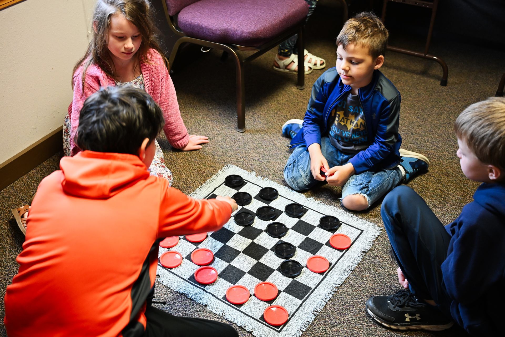 Children playing checkers on a floor mat in a classroom setting