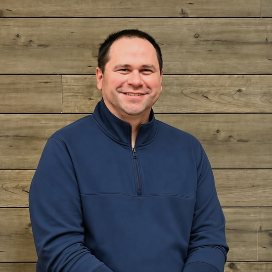 Smiling man in a navy pullover standing against a wooden wall