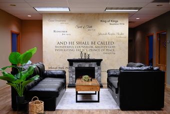 Modern lounge with black leather sofas, fireplace, coffee table, and large potted plant on a wood floor.