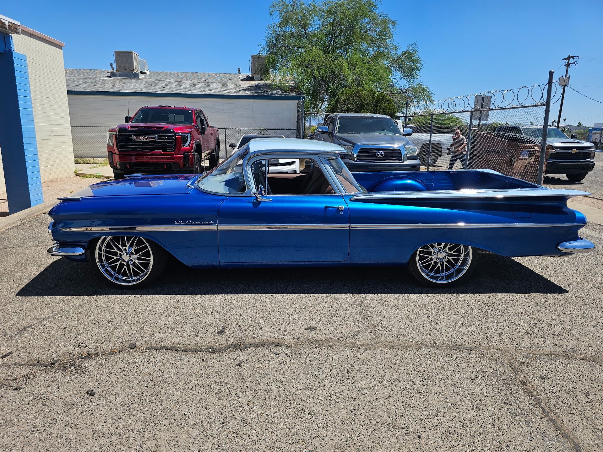 Blue classic car parked outdoors in sunlight, side view with chrome wheels and a white roof.