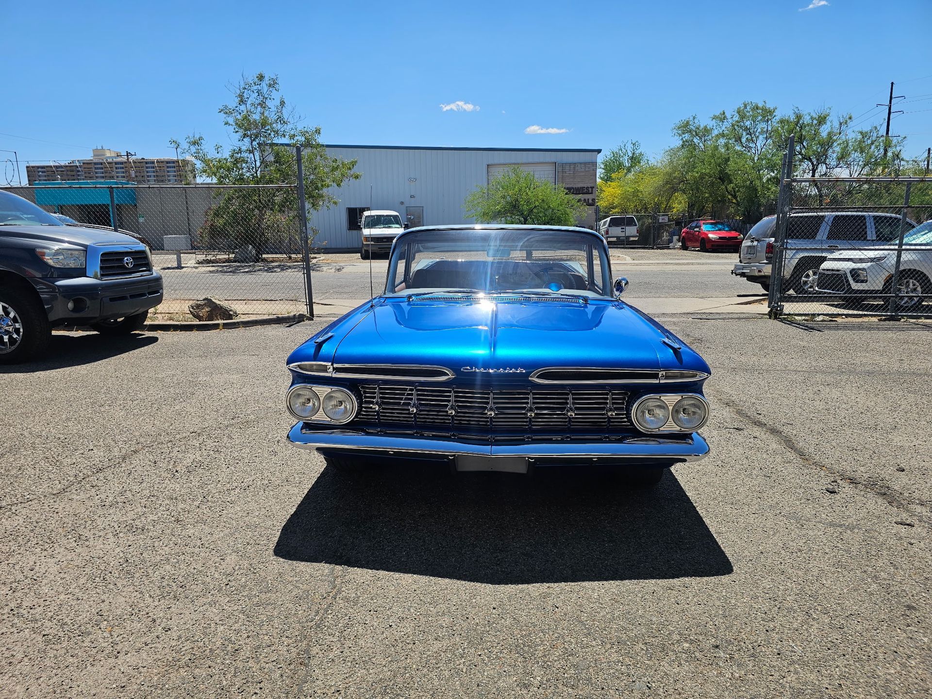 Bright blue vintage car parked in a gravel lot under a clear sky