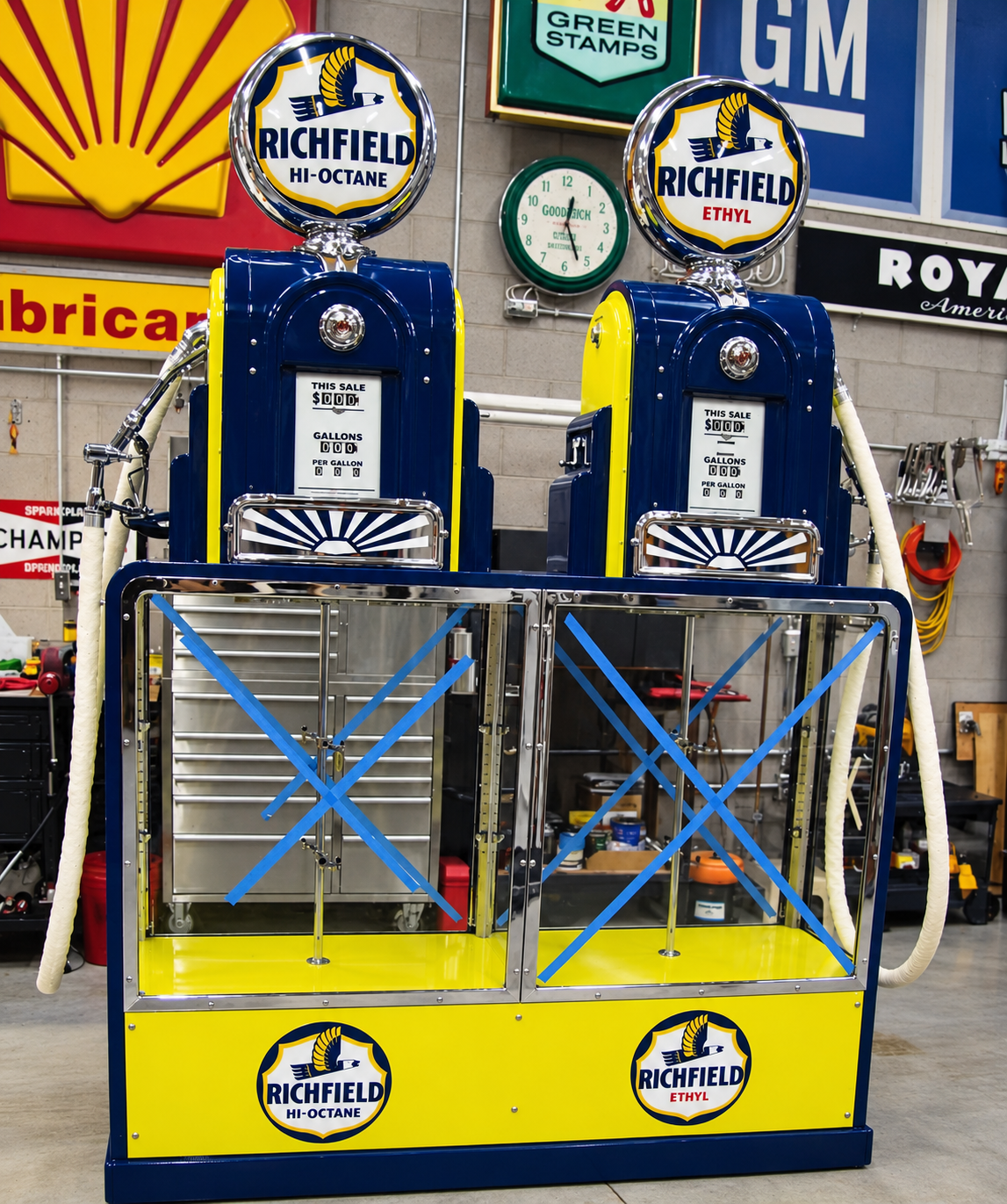 Two vintage blue gas pumps with yellow bases in a garage museum display
