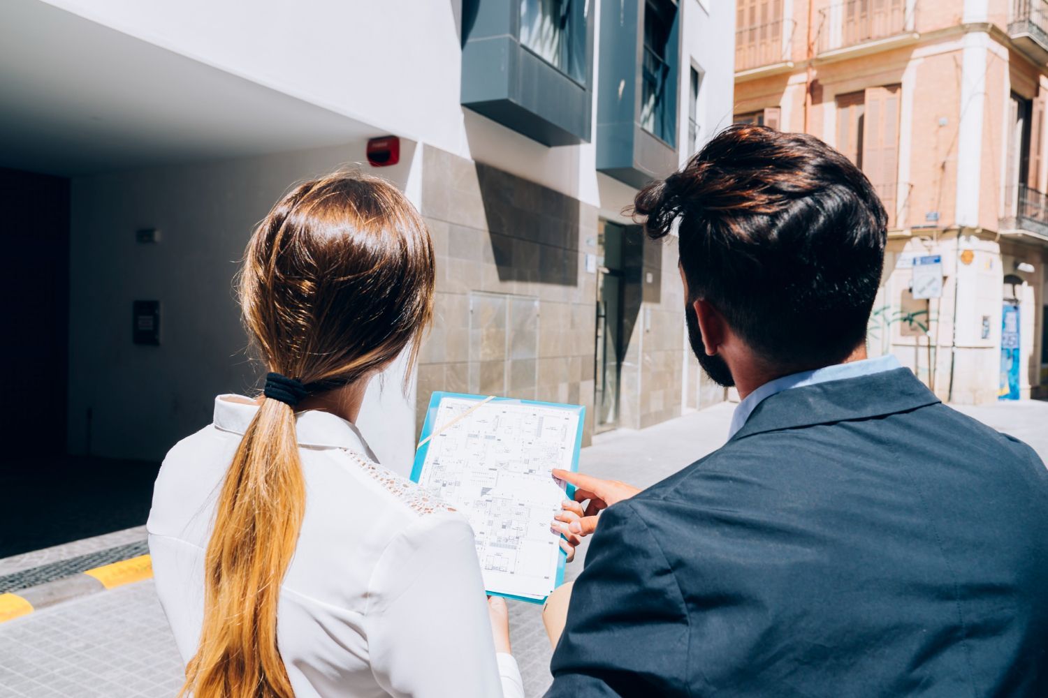 Two people study a map on a sunny city street beside tall buildings.