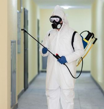Person in white hazmat suit spraying disinfectant in a hallway