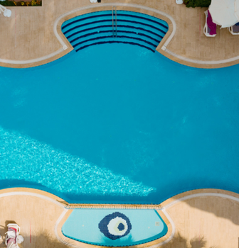 Overhead view of a blue swimming pool with curved edges, steps, and surrounding tan deck with umbrellas