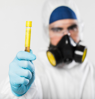 Gloved lab worker holding a yellow test tube while wearing a respirator and face shield