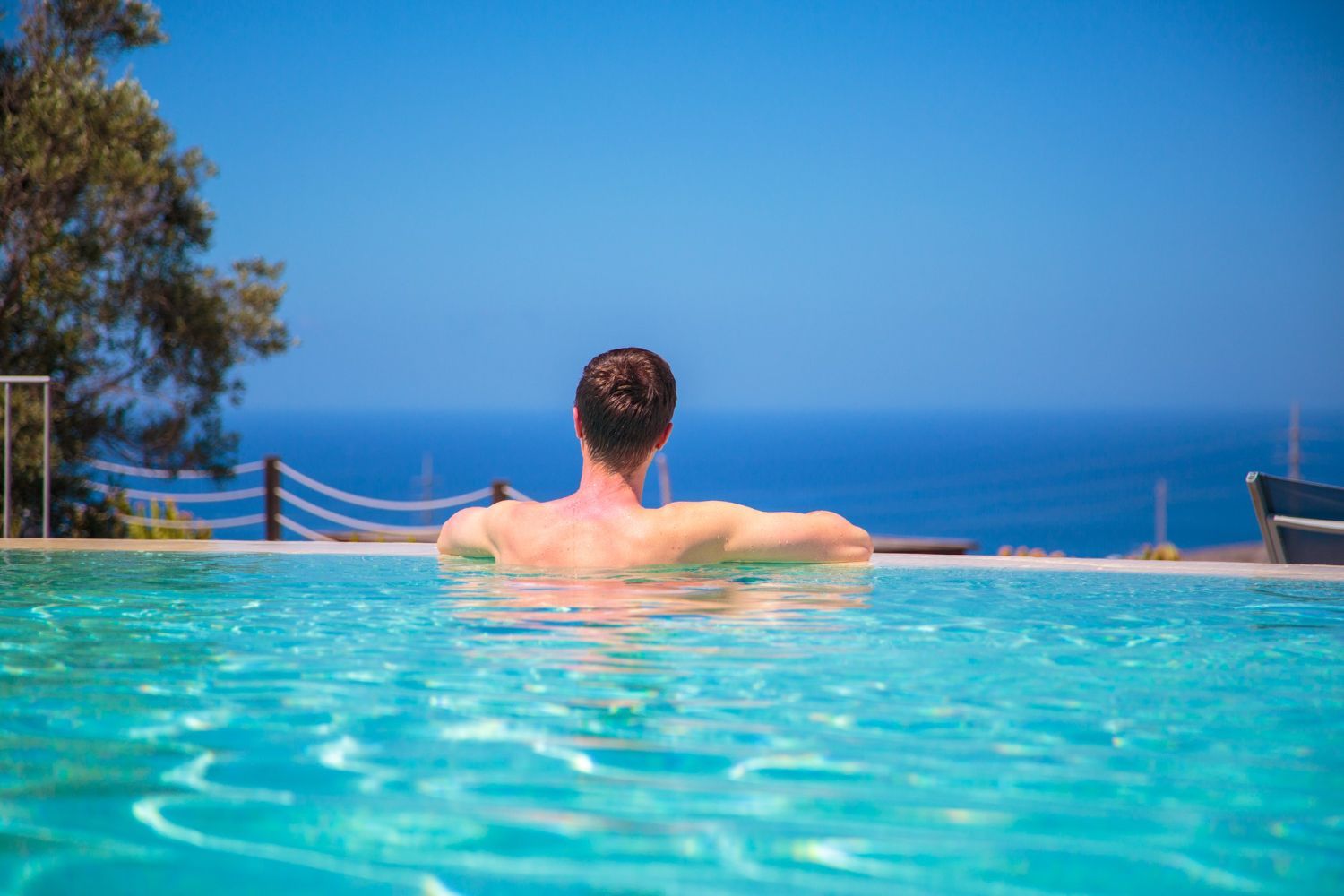 Person relaxing in an infinity pool overlooking the ocean and blue sky