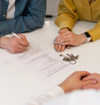 People signing a document at a table with keys and a smartwatch nearby