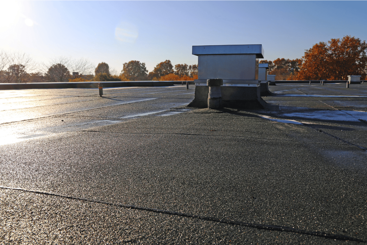 Rooftop with a small ventilation structure at sunset, wet surface reflecting light and autumn trees in the distance
