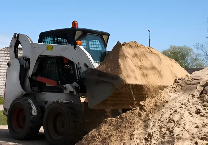 Skid-steer Loader Scoops Sand From a Pile Outside on a Sunny Day — Mount Isa Hire Service & Sales in Mount Isa City, QLD