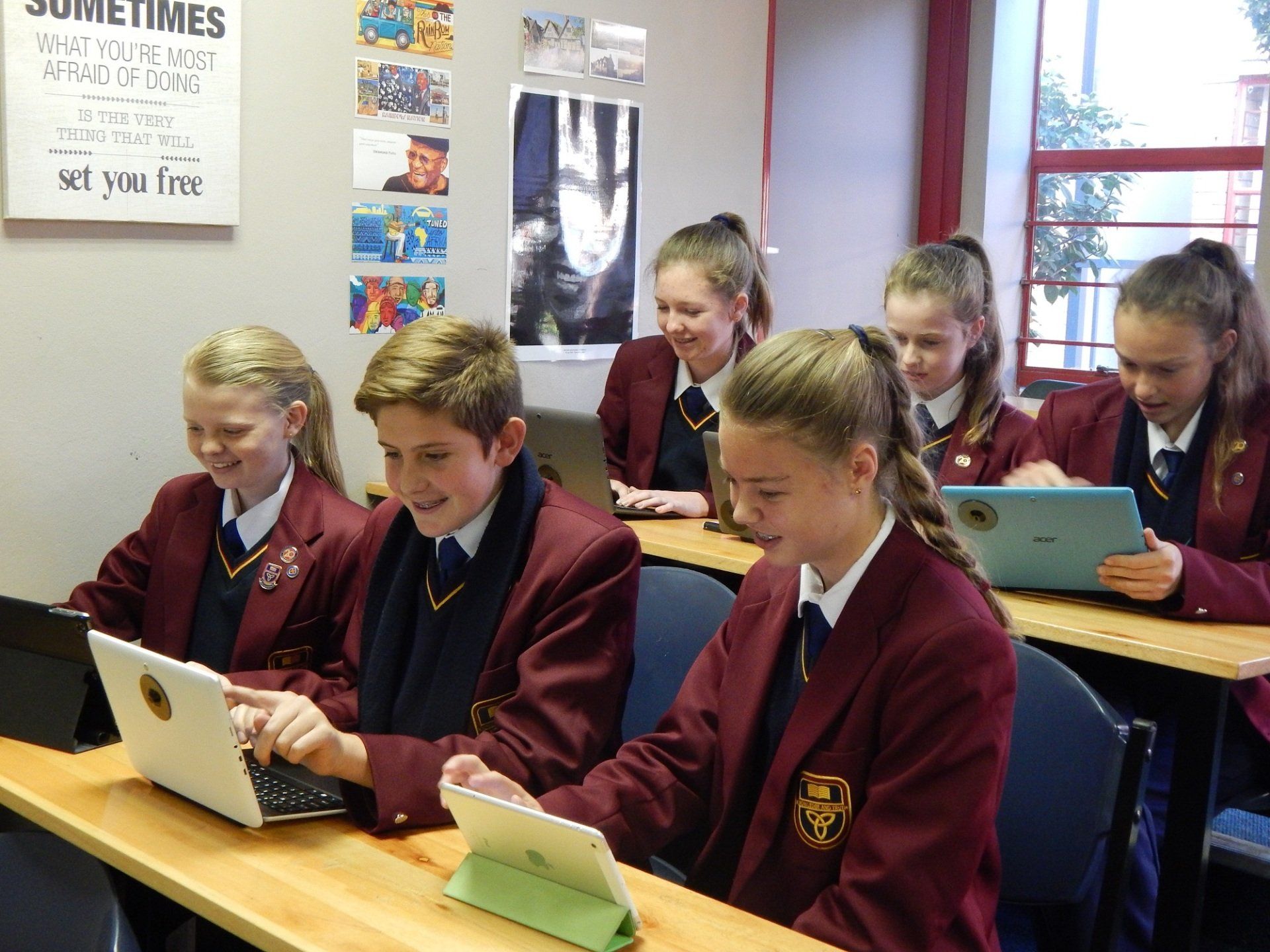 a group of children are sitting at desks in a classroom using laptops and tablets .