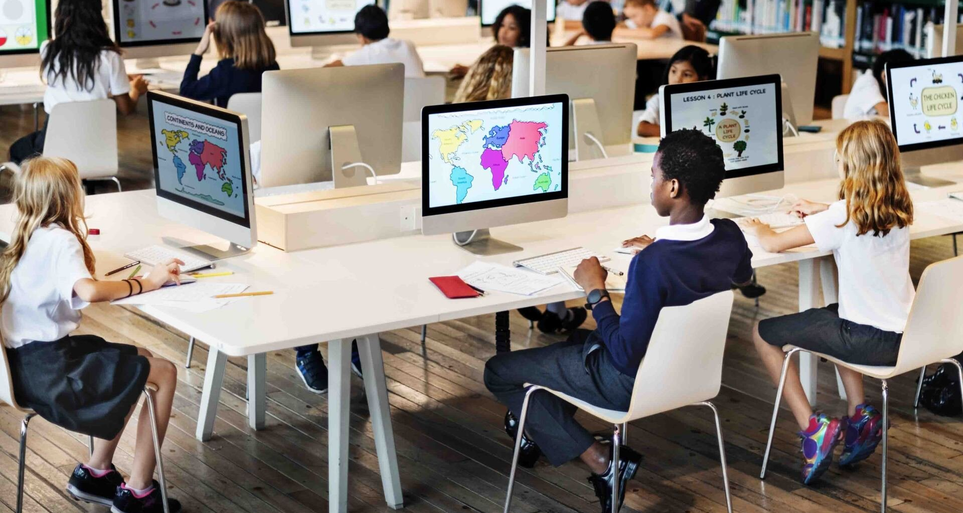 A group of children are sitting at tables in front of computers in a classroom.